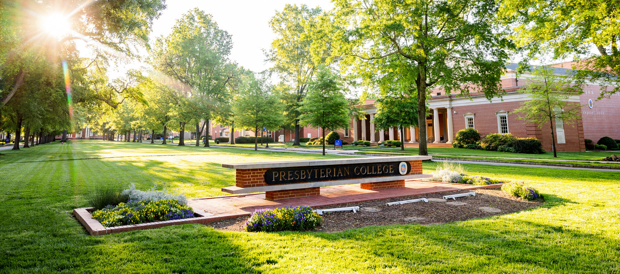 Picture of the Presbyterian College sign with sunlight peaking through the trees.