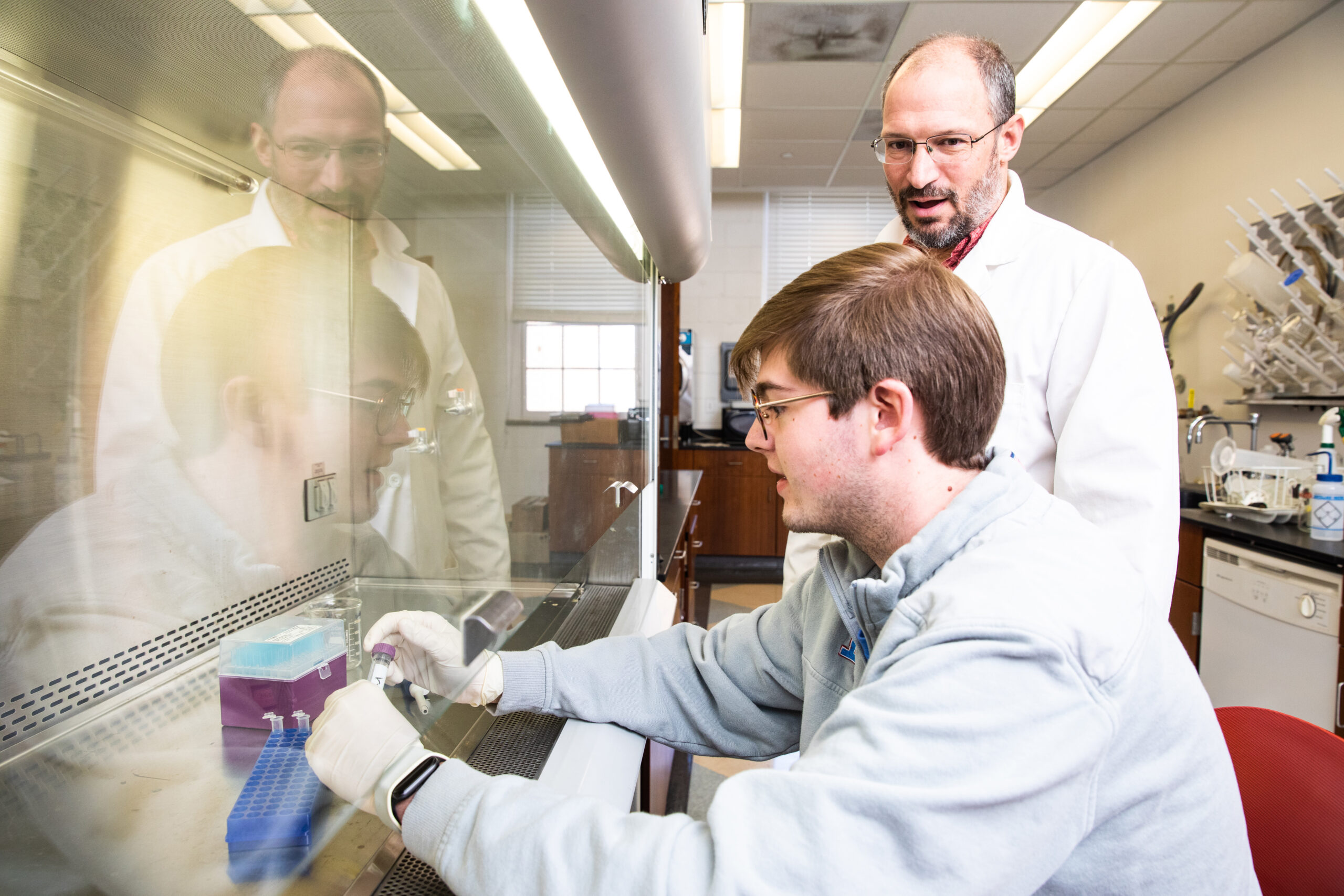 Student in science lab with professor over his shoulder