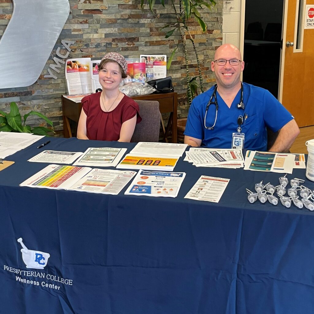 Two professors from the Pharmacy faculty sitting at the front desk with brochures and souvenirs