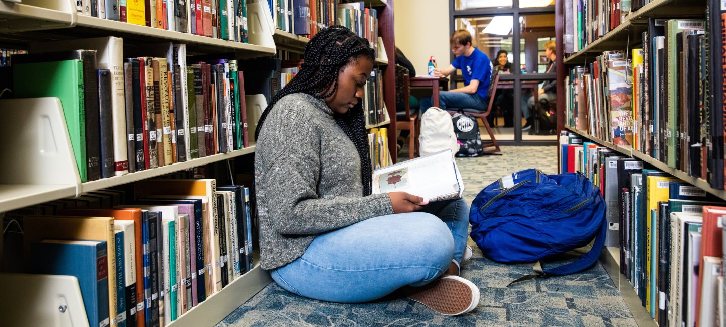 Student sitting and reading a book in Library at Presbyterian College.