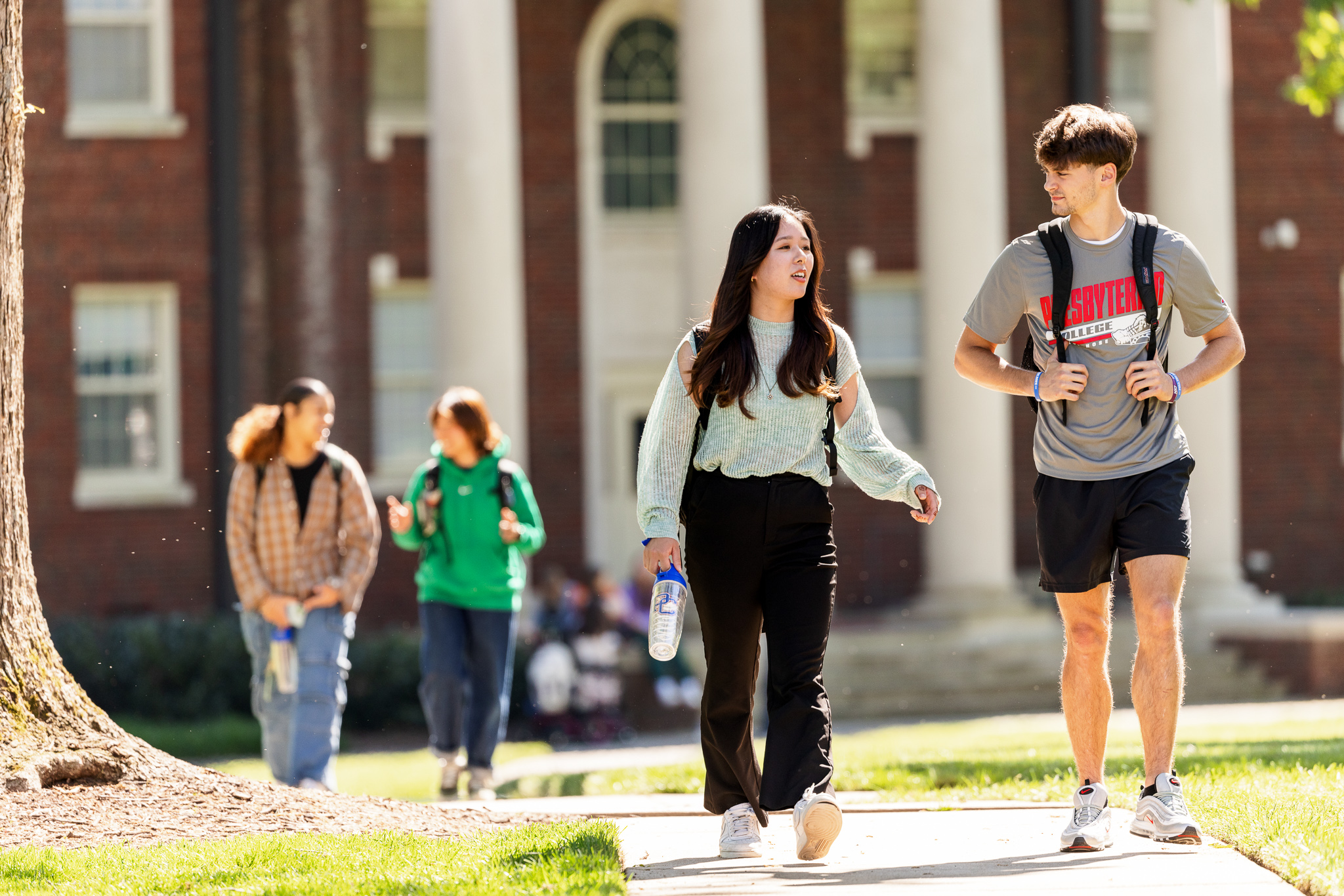 Presbyterian College students walking and talking on a sunny day in front of a historic campus building with white columns.