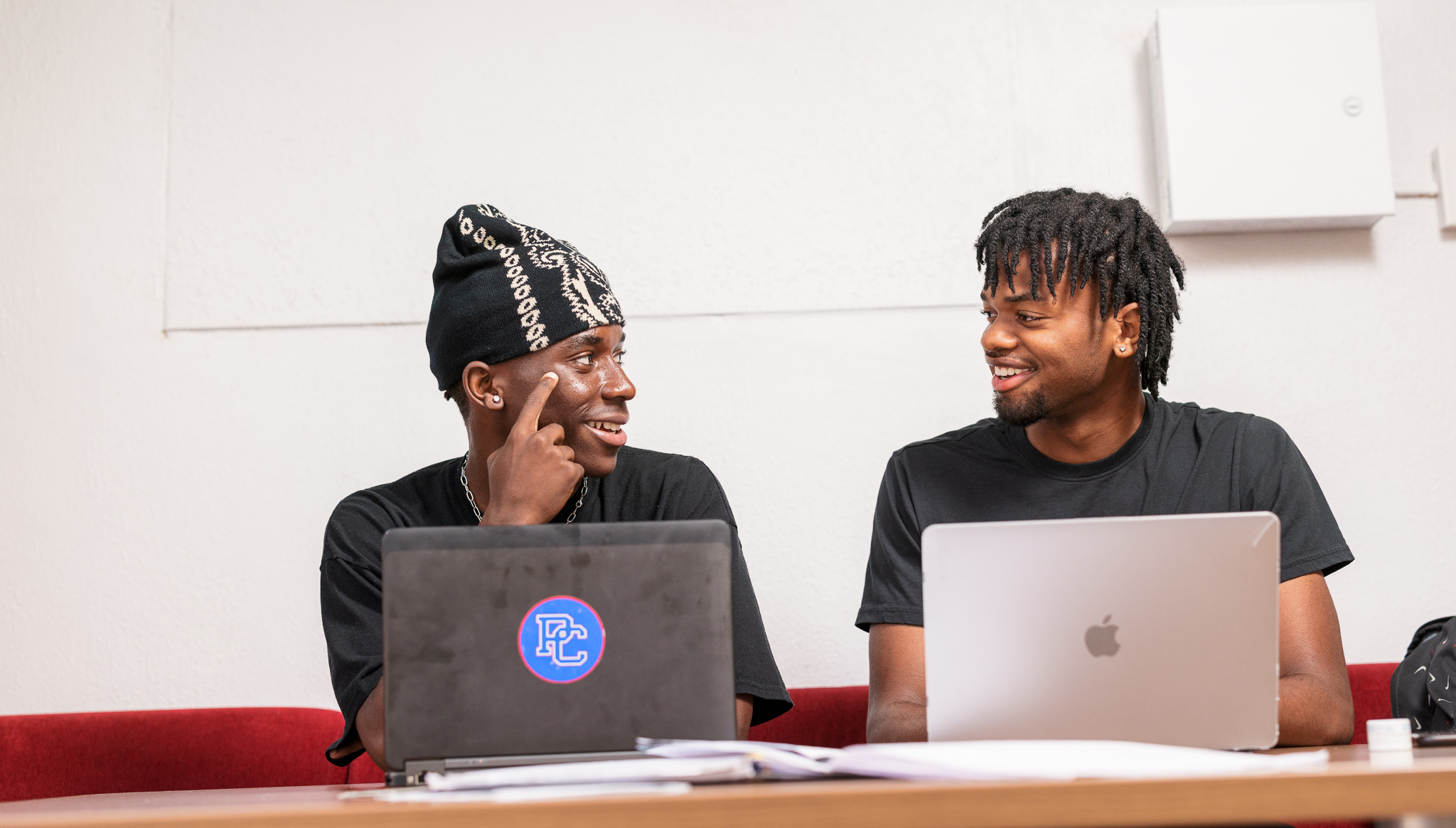 Two PC students talking and working on computers.